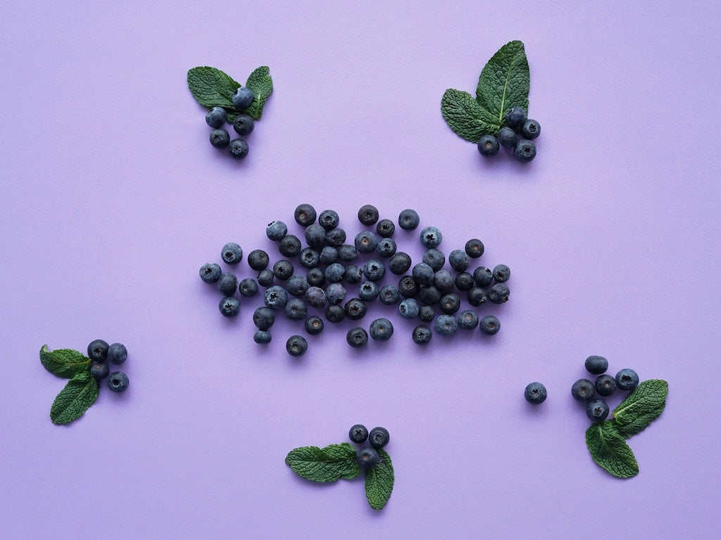 Blueberries and mint leaves are arranged on a purple surface.