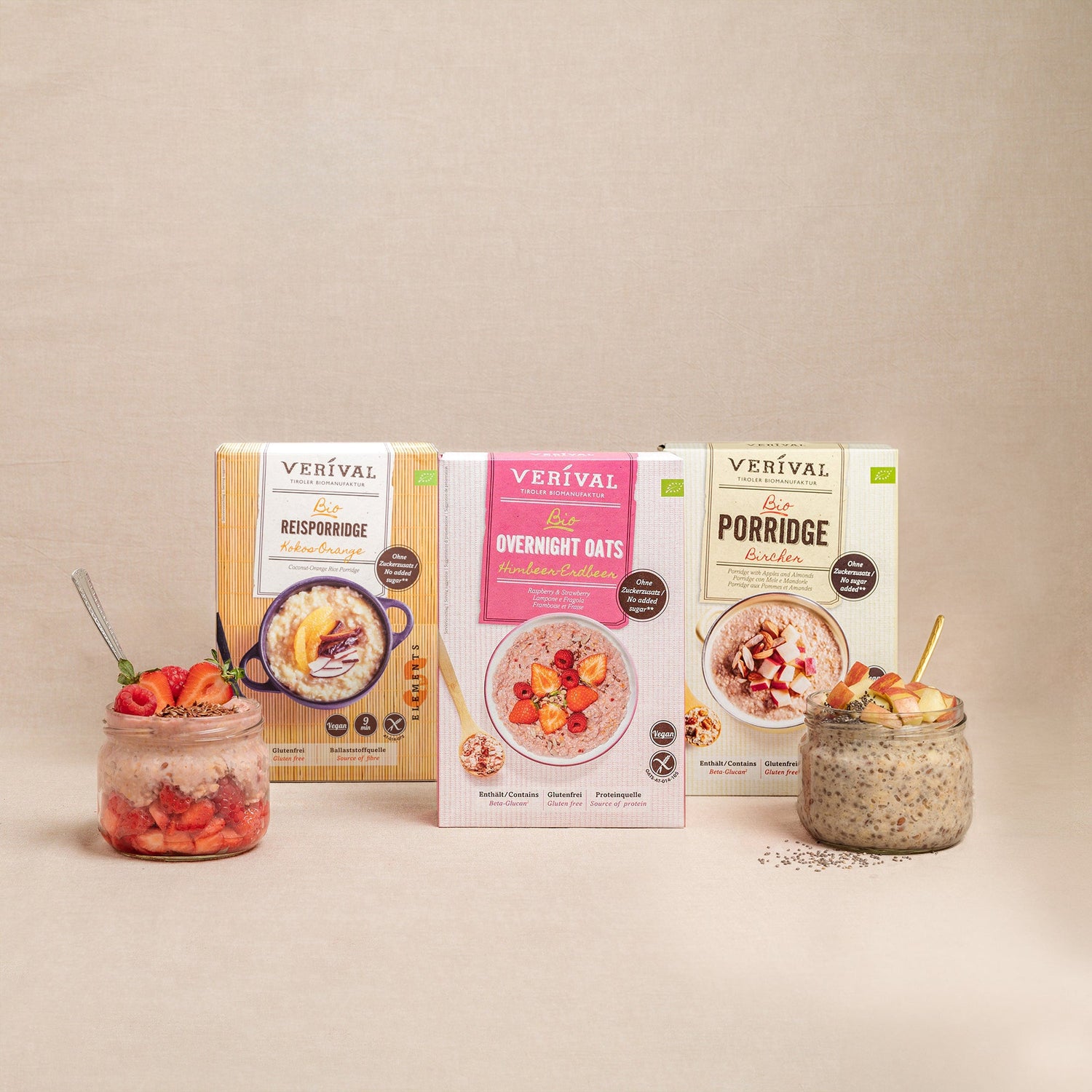 A breakfast scene with bowls of purple porridge, fresh blueberries, apple slices, a box of Verival porridge, a teapot, lemon slices, and a cup of coffee on a wooden table.
