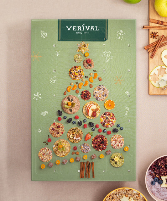Die Adventskalender-Box der Verival Bio GmbH zeigt eine grüne Schachtel mit Weihnachtsbaum-Motiv, gefüllt mit verschiedenen Trockenfrüchten, Nüssen, Vollkorn-Müsli-Stückchen und Bio-Frühstückssnacks in festlicher Verpackung.
