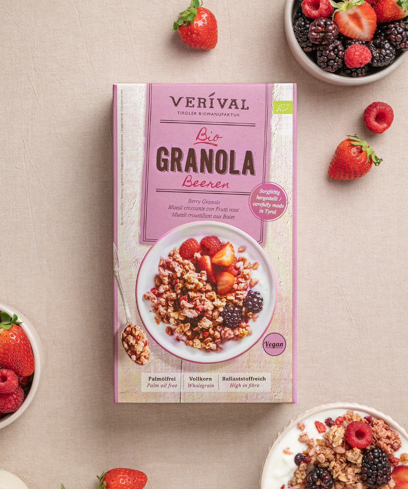 Auf einem beigen Untergrund präsentiert das „Best Breakfast Friends“-Set von Verival Bio Granola mit frischen Früchten. Um das Set herum befinden sich Schalen mit Granola und Beeren, verstreut mit Erdbeeren und Himbeeren – ideal für ein vollwertiges Frühstück oder als Ergänzung zum morgendlichen Porridge.