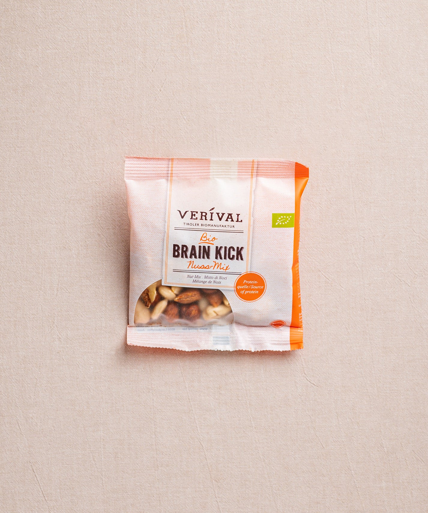 Auf beigem Hintergrund ist eine Packung Brain Kick Nussmischung der Verival Bio GmbH abgebildet, die hochwertige Bio-Nüsse hervorhebt, die als ein perfekter Energiespeicher dienen.