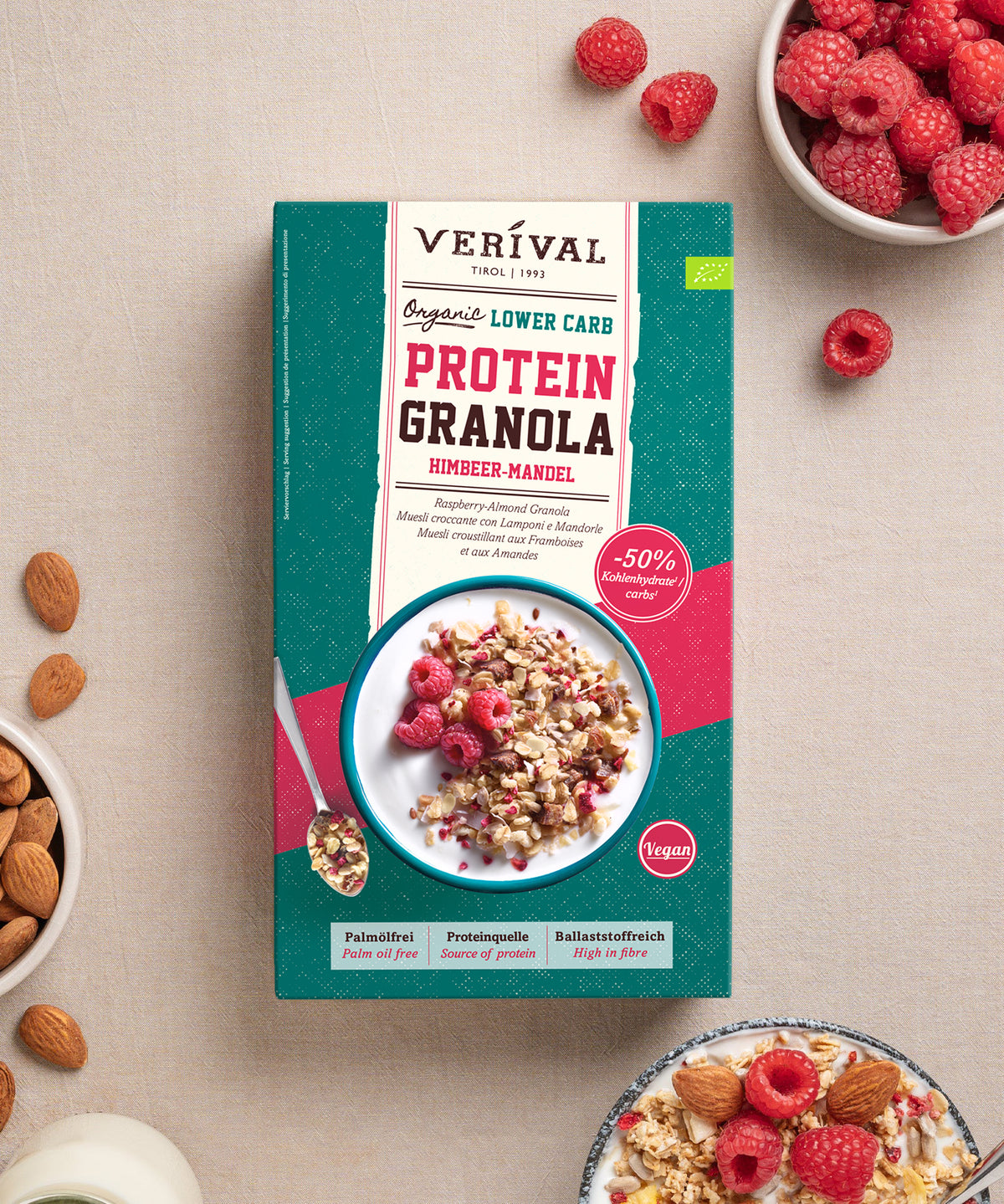 Die Verpackung des „Bio Protein Lower Carb Granola Himbeer-Mandel“ der Verival Bio GmbH auf beigem Hintergrund, auf der eine Schüssel mit Granola, Himbeeren und Mandeln abgebildet ist, hebt die pflanzlichen Proteine und den geringen Kohlenhydratgehalt des Produkts hervor.