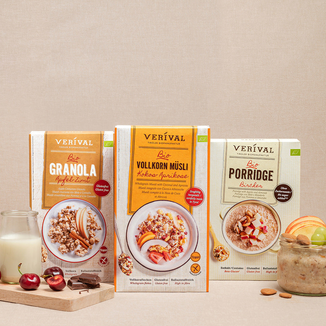 Three cereal boxes labeled Crunchy, Wholegrain Muesli, and Porridge are presented with a glass, cherries, and almonds on a beige background.
