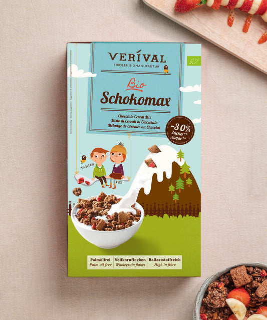 Auf dem Tisch steht eine Packung Schokomax von Verival Bio mit Comicfiguren und einem Schokoladenberg-Design. Es punktet mit Bio-Zutaten, 30 % weniger Zucker und einer palmölfreien Rezeptur. 