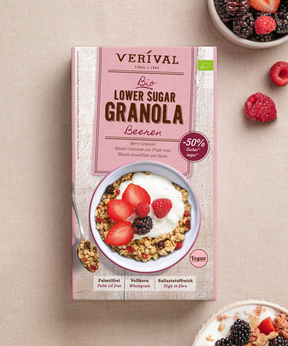 Auf einer hellen Unterlage steht eine Packung „Bio Lower Sugar Beeren-Müsli“ der Verival Bio GmbH; davor steht eine Schüssel mit Müsli, Joghurt und frischen Beeren, und oben rechts steht eine kleine Schüssel mit gemischten Beeren.