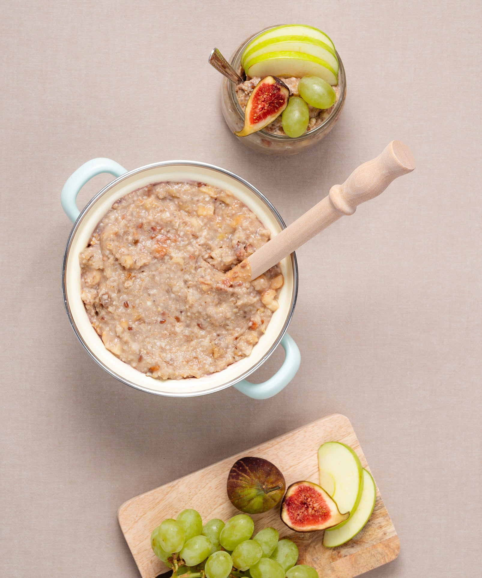 Ein cremiges Porridge mit Nüssen und ein Verival Porridge Spurtle von Anton Gruber stehen neben einem Brett mit Trauben, Feigen und Apfelspalten. 