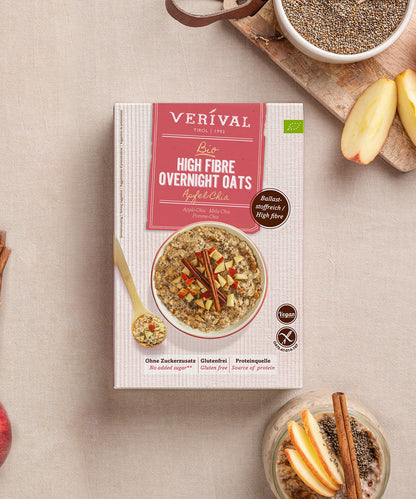 Eine Dose Verival Bio GmbH Bio High Fibre Oats Apfel-Chia steht auf einer hellen Fläche, umgeben von einer Schale mit veganen Haferflocken, Apfelscheiben, Zimtstangen und Chiasamen - reich an Ballaststoffen.