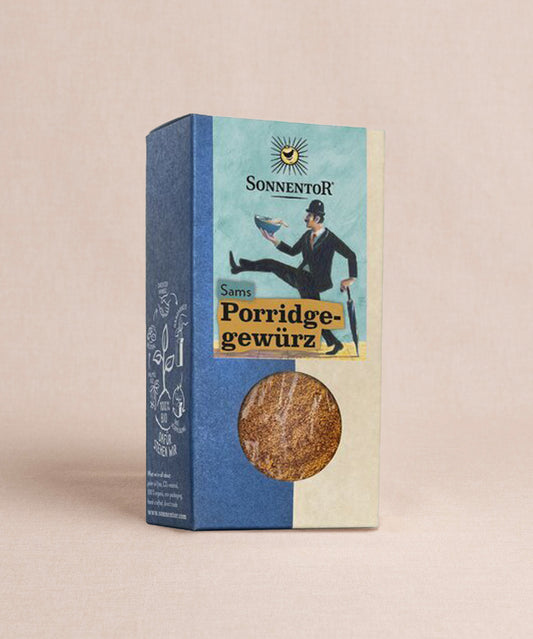Eine Schachtel Sonnentor Porridge Gewürz ist vor einem schlichten Hintergrund zu sehen. Ein rundes Sichtfeld gibt den Blick auf das Gewürz frei, während verspielte Grafiken die blau-beige Verpackung zieren.