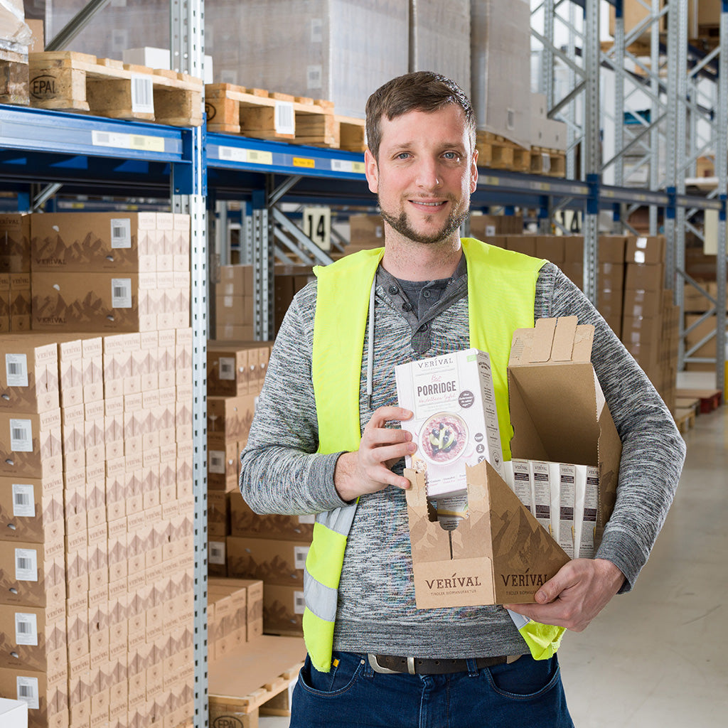 Ein Verival-Mitarbeiter vor einem Warenregal zeigt eine Porridgepackung.